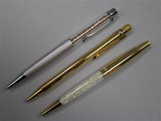 A Must de Cartier gilt ballpoint pen and two Swarovski ballpoint pens.